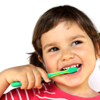 Ein kleines, dunkelhaariges Mädchen mit rotem Pullover putzt sich mit einer grünen Zahnbürste die Zähne.